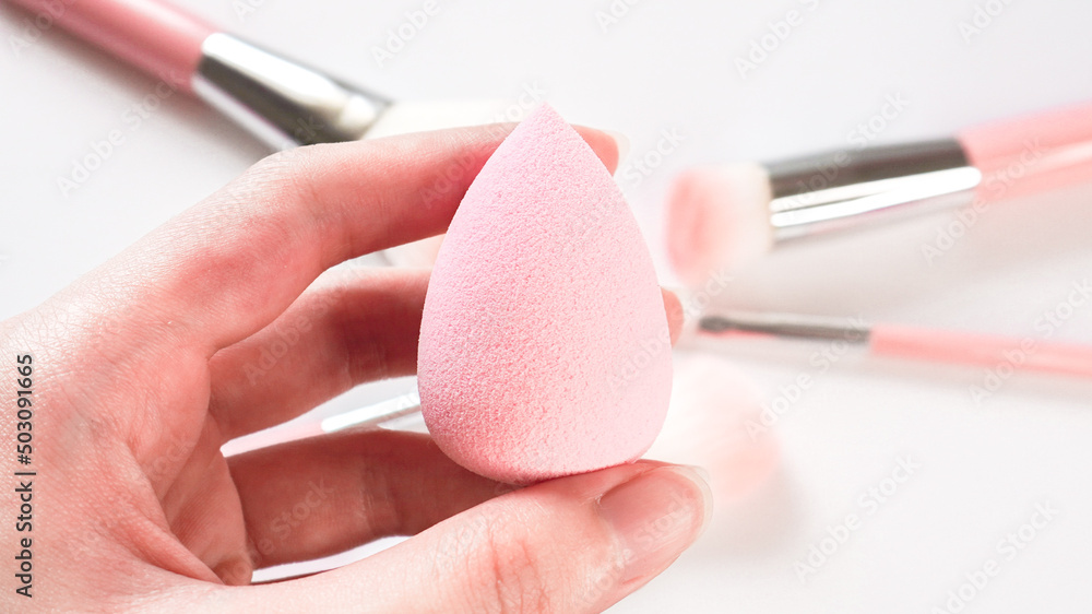 Canvas Prints woman's hand holding a clean makeup sponge with blurred make up brushes in the background