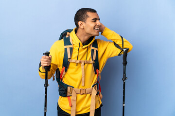 African American man with backpack and trekking poles over isolated background listening to something by putting hand on the ear