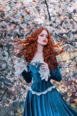 Fantasy portrait red-haired girl romantic princess stands in spring flowering garden. Blooming...