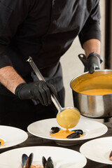 chef prepares carrot cream soup with seafood in a restaurant