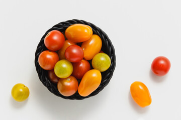 Cherry tomatoes in black basket on white background.