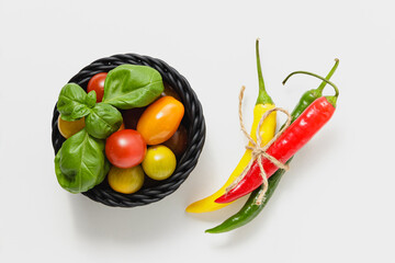 Cherry tomatoes in black basket and green basil leaves on white background.
