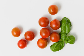 Cherry tomatoes with green basil on white background.