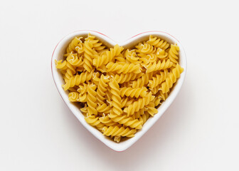 Raw pasta fusilli in heart bowl.