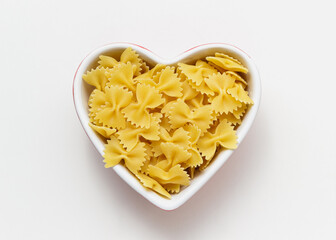 Raw pasta farfalle in heart bowl.