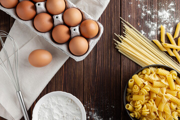 Different kinds of raw pasta with eggs on wooden background.