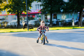 stylish European boy in shirt and jeans rides balance bike on asphalt. Child riding without helmet