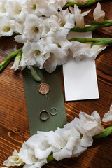 Wedding stationery top view. Flat lay blank white invitations, green envelopes, wedding decorations and fresh gladiolus flowers on natural wooden background.
