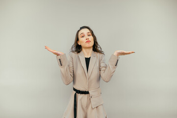 Confused woman in a suit stands on a beige background and looks puzzled at the camera and spreads his arms.