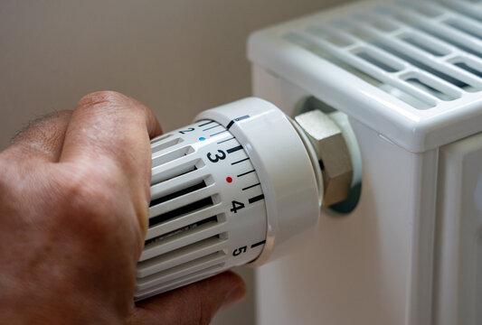 Steigende Heizkosten und Ölpreise in der Krise: Mann regelt Temperatur zuhause mit dem Heizungsthermostat runter um zu Energie sparen