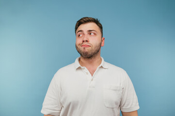 A cunning man in a white T-shirt stands on a blue background and looks away with a sly smile