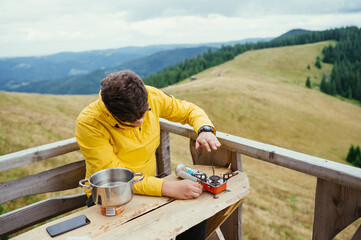 A man sits at a table on the terrace of a house in the mountains and prepares to eat against the backdrop of a mountain landscape.