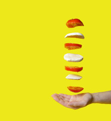 flying tomato and mozzarella isolated on yellow background. frozen motion. mozzarella and tomato soar over hand. copy space