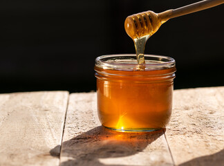 honey jar on wooden table and dark backgroun, honey dripping from honey dipper