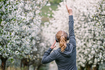 Happy woman with headphones listening music and dancing outdoors in spring nature. Enjoyment and...