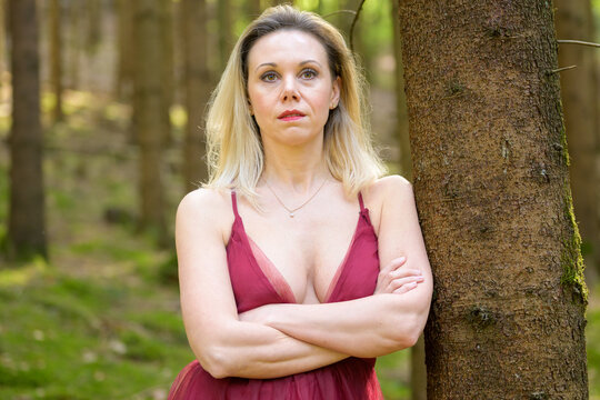 Woman in dress revealing cleavage posing in forest.