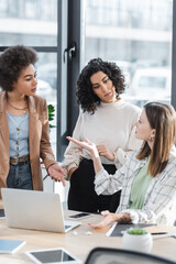 Blurred businesswoman pointing with hand near multiethnic colleagues and gadgets in office.
