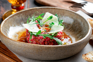 Beef tartare with dried tomatoes decorated with parmesan and arugula is served in a plate on a wooden table, close up
