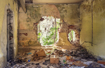 interior room of dilapidated abandoned house with broken wall with brick holes and garbage on the floor - war horror scene