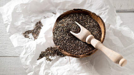 Chia seeds in coconut bowl with wooden spoon on white wooden background, top view