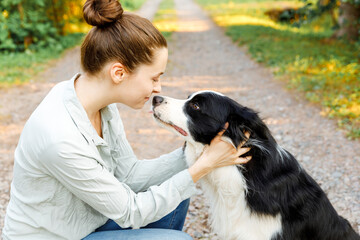 Naklejka na ściany i meble Smiling young attractive woman playing with cute puppy dog border collie on summer outdoor background. Girl holding embracing hugging dog friend. Pet care and animals concept.
