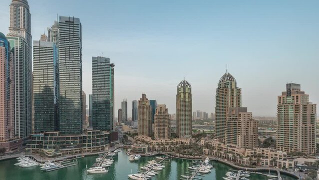 Dubai marina tallest skyscrapers and yachts in harbor aerial day to night transition timelapse after sunset. View at apartment buildings, hotels and office blocks, modern residential development of