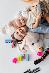 top view of cheerful woman and toddler son lying on huge soft toy on white.