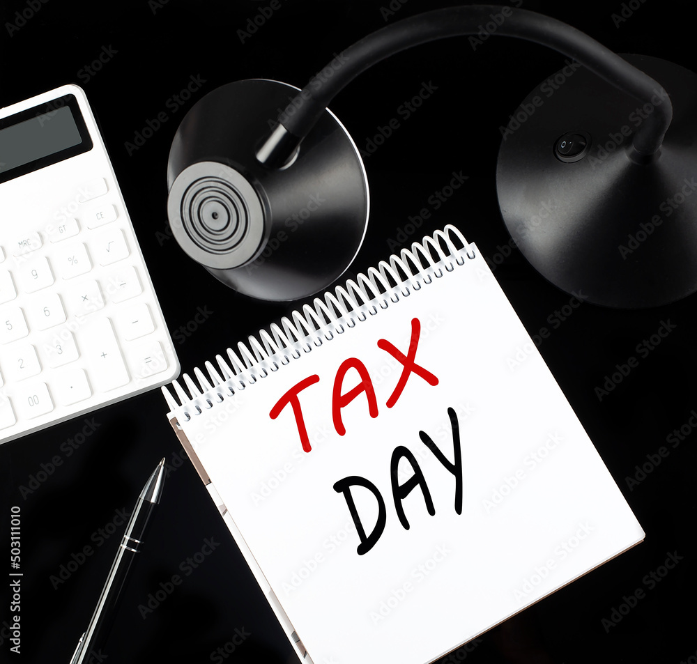 Poster opened paper notebook with text tax day with a pen, calculator and table lamp on black background.