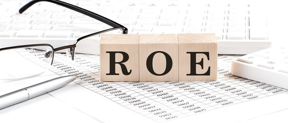 ROE written on wooden cube with keyboard , calculator, chart,glasses.Business concept