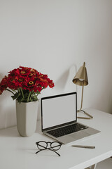 Laptop computer with blank copy space screen on table decorated with stationery, flowers bouquet, lamp. Aesthetic minimalist home office workspace. Online shop, store mockup template