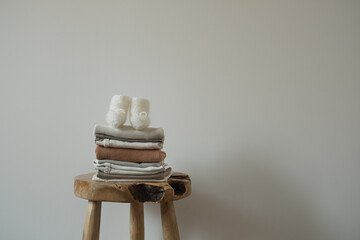 Aesthetic Scandinavian newborn baby clothes, socks stack on stylish stool against white wall....