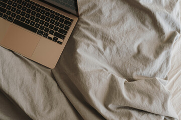 Laptop computer on bed with neutral bed linens. Top view minimalist aesthetic luxury bohemian workspace. Flatlay