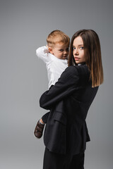 young businesswoman and her little son looking at camera isolated on grey.