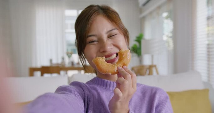 Young vlogger asia people influencer girl take photo eat bite smiley donut funny face post review on instagram tiktok reel app. Sweet tooth food sugar lover enjoy fun show viral video camera at home.