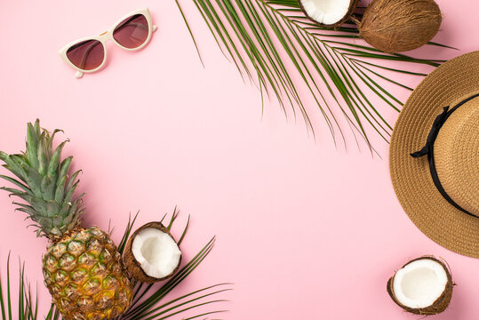 Summer weekend concept. Top view photo of sunhat sunglasses coconuts pineapple and palm leaves on isolated pastel pink background with copyspace in the middle