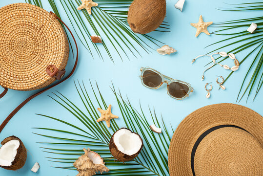 Summer weekend concept. Top view photo of round rattan bag sunhat sunglasses coconuts starfishes shell bracelet earrings and palm leaves on isolated pastel blue background