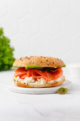 Bagel sandwich with salmon, cream cheese and green leaves on marble board and white background. Burger with salmon.