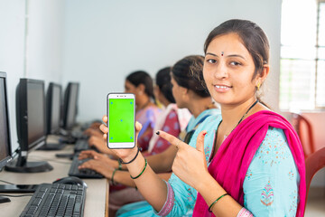 Happy women showing green screen mobile phone by pointing finger while lookingcamera at computer...