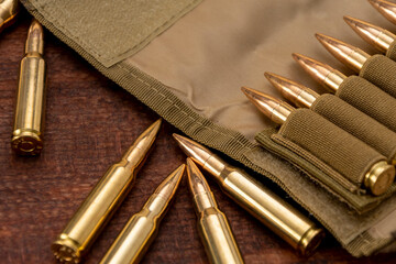 Military bandolier with yellow live ammunition cartridges of 7.62 caliber on a wooden background.