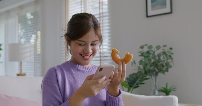 Young vlogger asia people influencer girl take photo eat bite smiley donut funny face post review on instagram tiktok reel app. Sweet tooth food sugar lover enjoy fun show viral video camera at home.