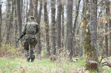 The figure of a man from the back walking in a camouflage green uniform with ammunition with...