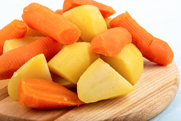 Close-up of boiled potatoes and carrots on a wooden cutting board.