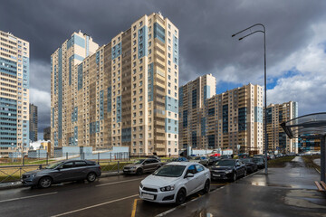 Multi-apartment residential buildings along the street, illuminated by the bright sun facades, against the background of a sky with dark clouds.