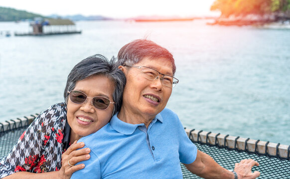 Happy Asian old elax easy senior retire woman and man couple, husband and wife lifestyle sitting near beach on vacation. People and business concept.