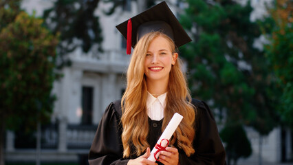 Beautiful with a large smile lady graduate posing in front of the camera while holding her diploma in the college garden