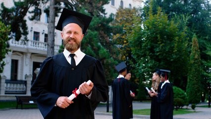 Charismatic man in the college garden posing in front of the camera after his graduation he wearing...