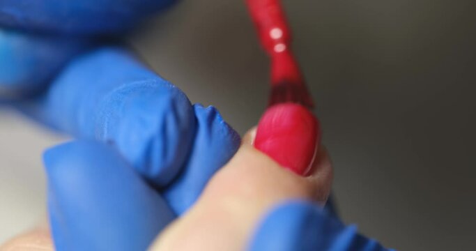 Manicurist paints client nails with bright red polish