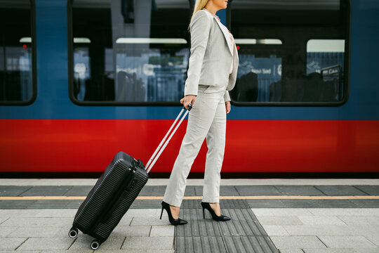 A middle-aged businesswoman with suitcase in her hand standing at the train station and waiting for her train to arrive.