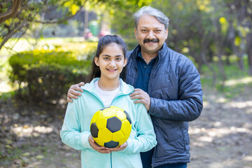 Portrait of young teenager female soccer player and mature male coach standing together in the park, Smiling asian sporty girl kid play outdoor game and activity with his trainer. Winter season. 