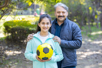 Portrait of young teenager female soccer player and mature male coach standing together in the...